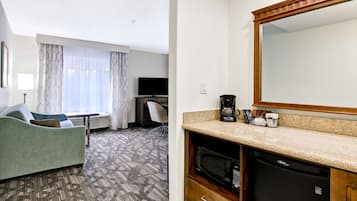A hotel room with a green sofa, a television, a desk, a coffee maker, and a microwave.