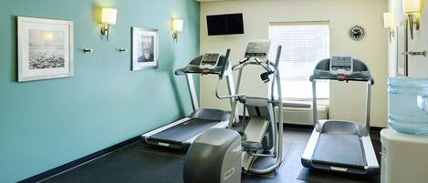 Un gimnasio con cintas de correr, bicicleta estática y dispensador de agua.