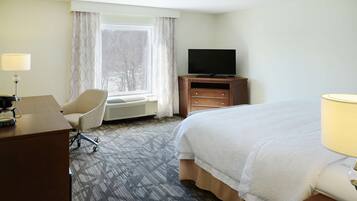 A hotel room with a bed, a desk with a lamp, a chair, a television on a wooden cabinet, and a window with curtains.