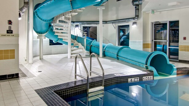 A swimming pool with a blue water slide, a starting hot tub, and a tiled floor. - Hampton Inn & Suites Saint John (Saint John)