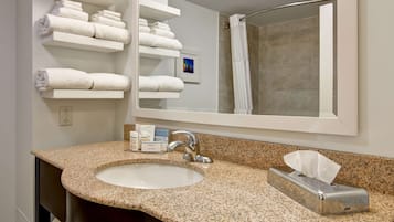 A bathroom with a granite countertop sink, a mirror, and shelves with folded towels.