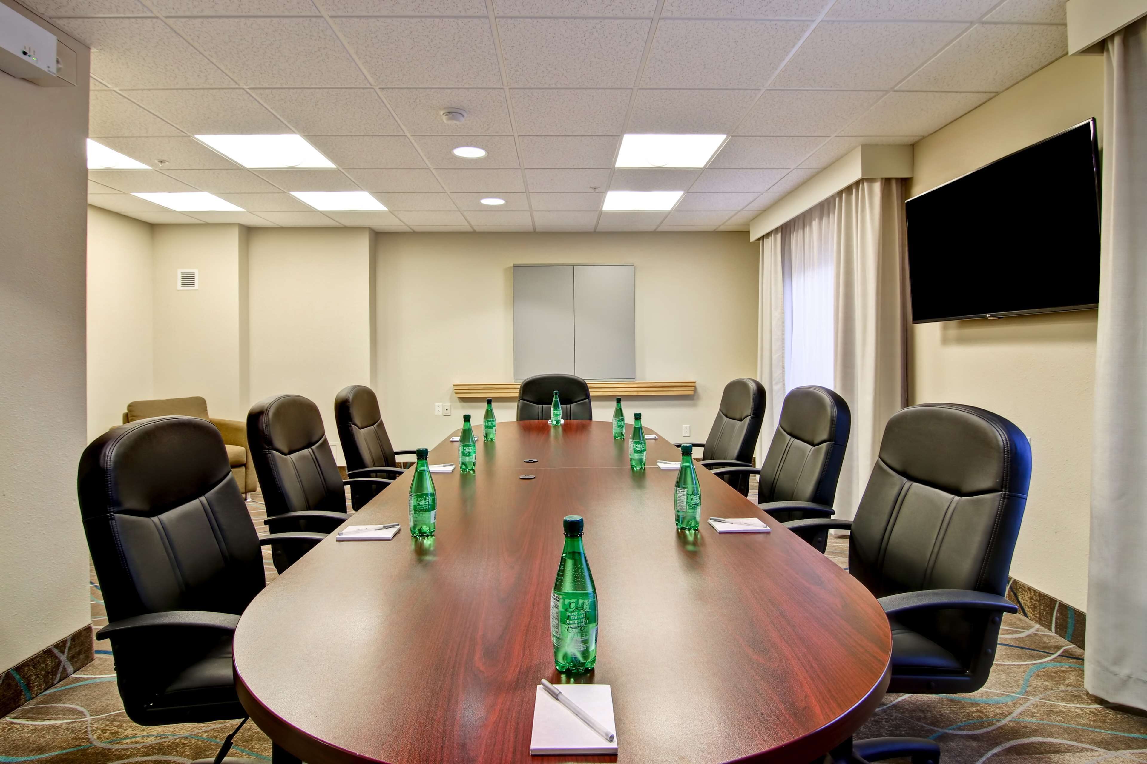 A conference room with a long wooden table, black leather chairs, and green water bottles.