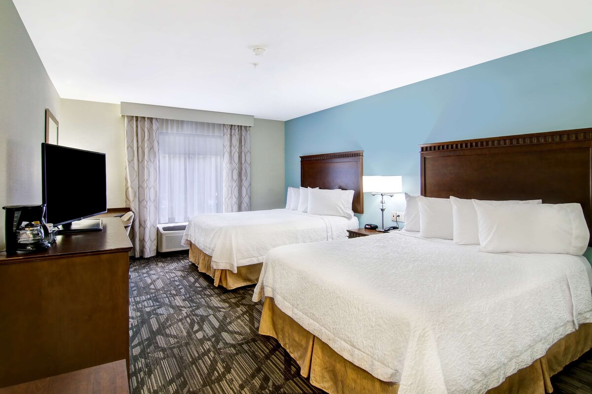 A hotel room with two beds, a desk with a TV, and a window with curtains.