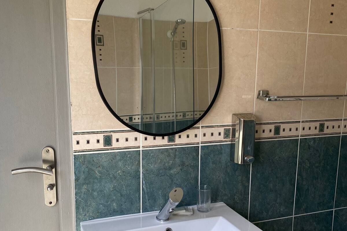 Ein Badezimmer mit einem weißen Waschbecken, einem runden Spiegel und einer Dusche.