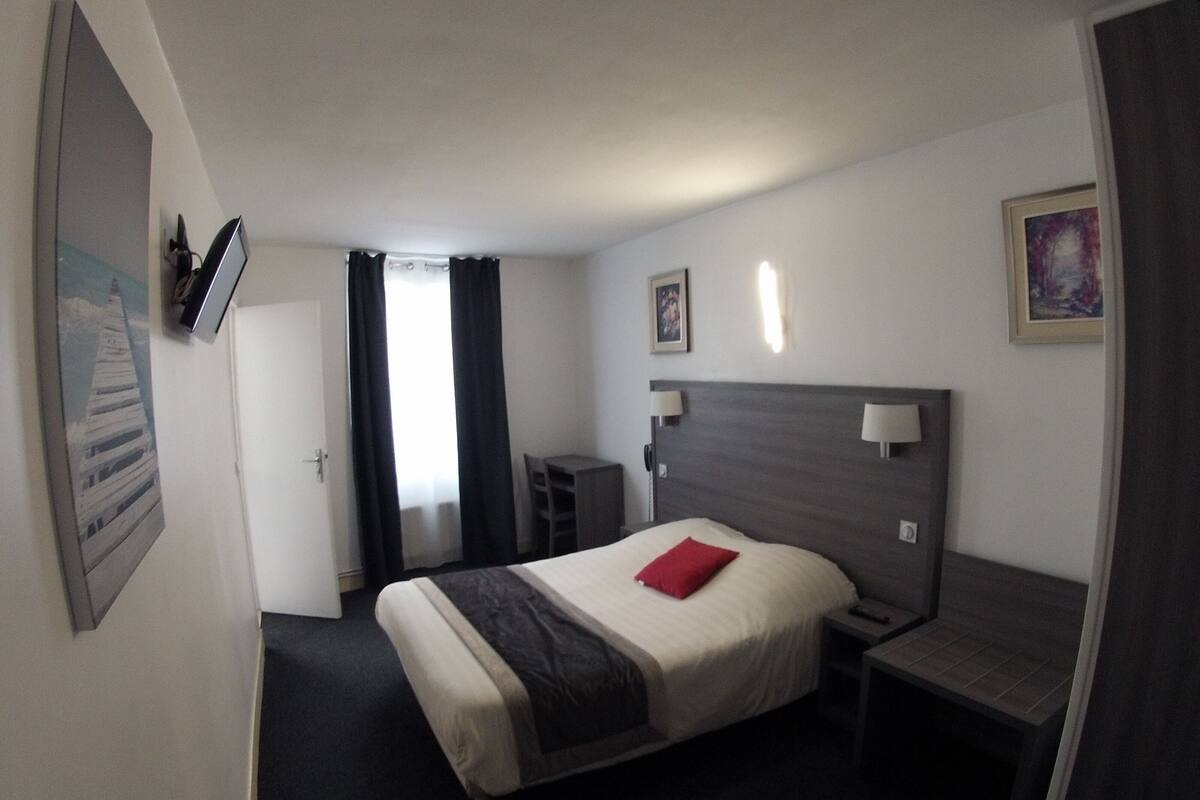 Ein Hotelzimmer mit Bett, Nachttisch, Stuhl, Schreibtisch und einer Tür.