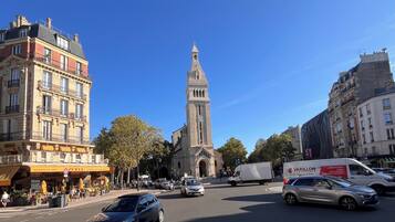 A street view with a prominent church tower, a café with outdoor seating, and various vehicles on the road.