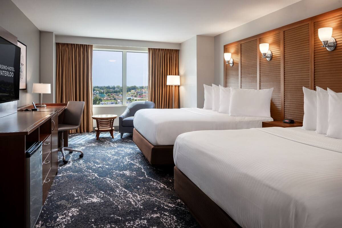 Ein Hotelzimmer mit zwei Betten, einem Schreibtisch, einem Stuhl, einem Fernseher und einem Fenster mit Vorhängen.