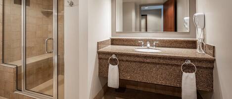 A modern bathroom with a glass shower enclosure, granite countertop, and a large mirror.