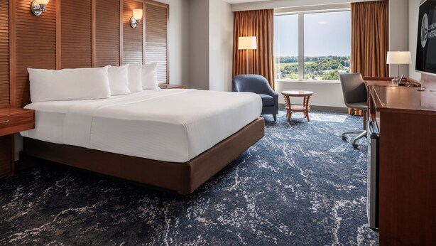 A hotel room with a large bed, a desk, a chair, and a view of the city. - Isle Casino Hotel Waterloo - A Caesars Rewards Destination (Waterloo)