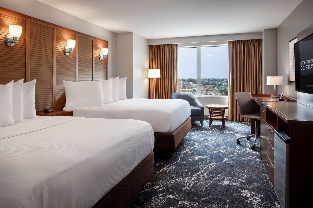 Ein Hotelzimmer mit zwei Betten, einem Schreibtisch, einem Sessel, einem Fernseher und einem Fenster mit Blick.