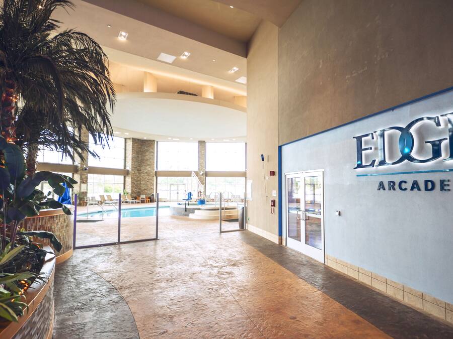 A spacious indoor area with a pool, palm trees, and a sign for 'EDGE ARCADE'.