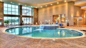 Una amplia piscina interior con un jacuzzi, sillas de descanso y vistas al exterior.