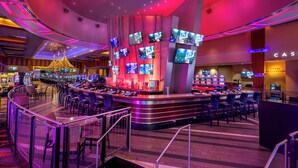 Un casino con múltiples mesas de juego y una zona de bar con varias pantallas.