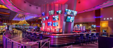 Ein Casino mit mehreren Spieltischen und einer Bar, die mit mehreren Bildschirmen ausgestattet ist.
