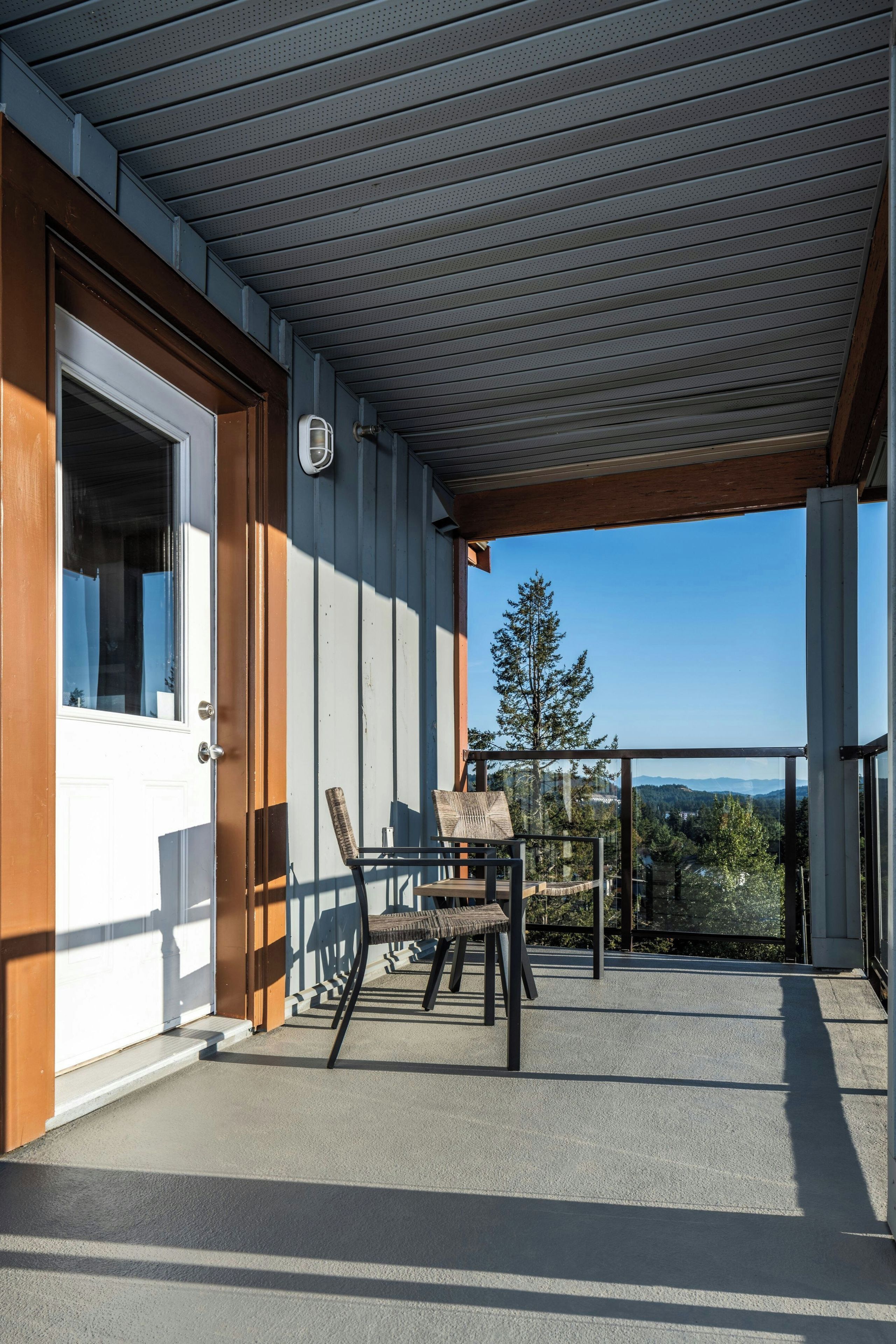 Un espacio al aire libre techado con un banco de madera y una mesa, una puerta, y vistas a árboles y montañas.
