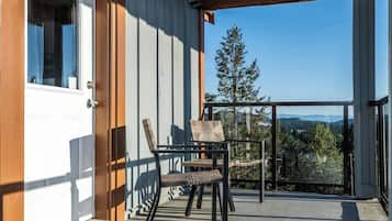 Un espacio al aire libre techado con un banco de madera y una mesa, una puerta, y vistas a árboles y montañas.