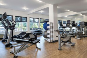 Un gimnasio con diverso equipamiento de ejercicio, amplias ventanas y suelo de madera.