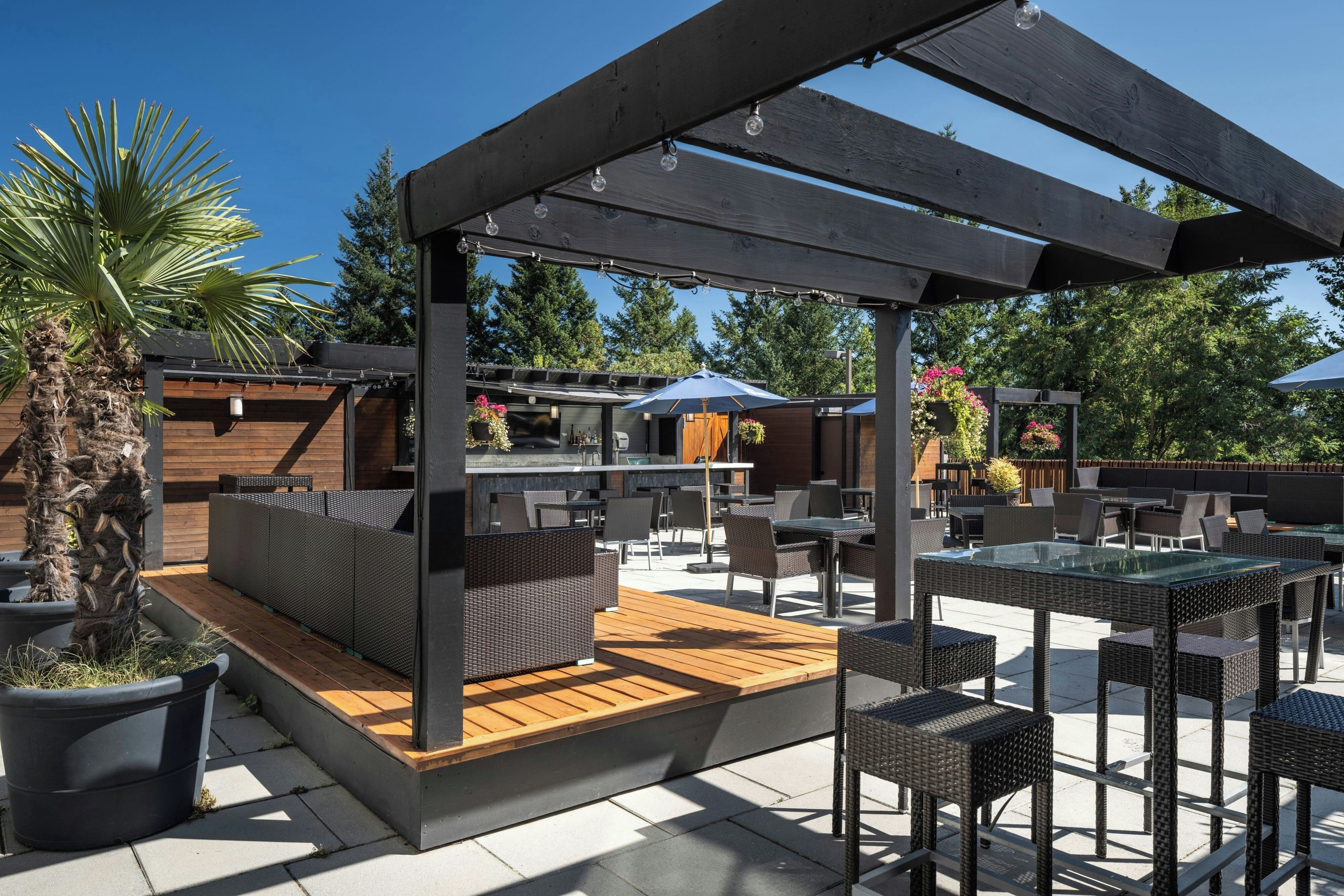 An outdoor patio with wooden flooring, wicker furniture, and a pergola structure.