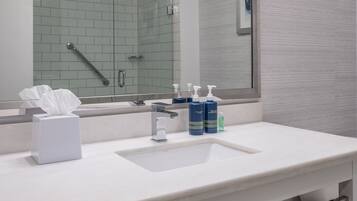 A modern bathroom with a large mirror, white sink, and a red basket with towels.