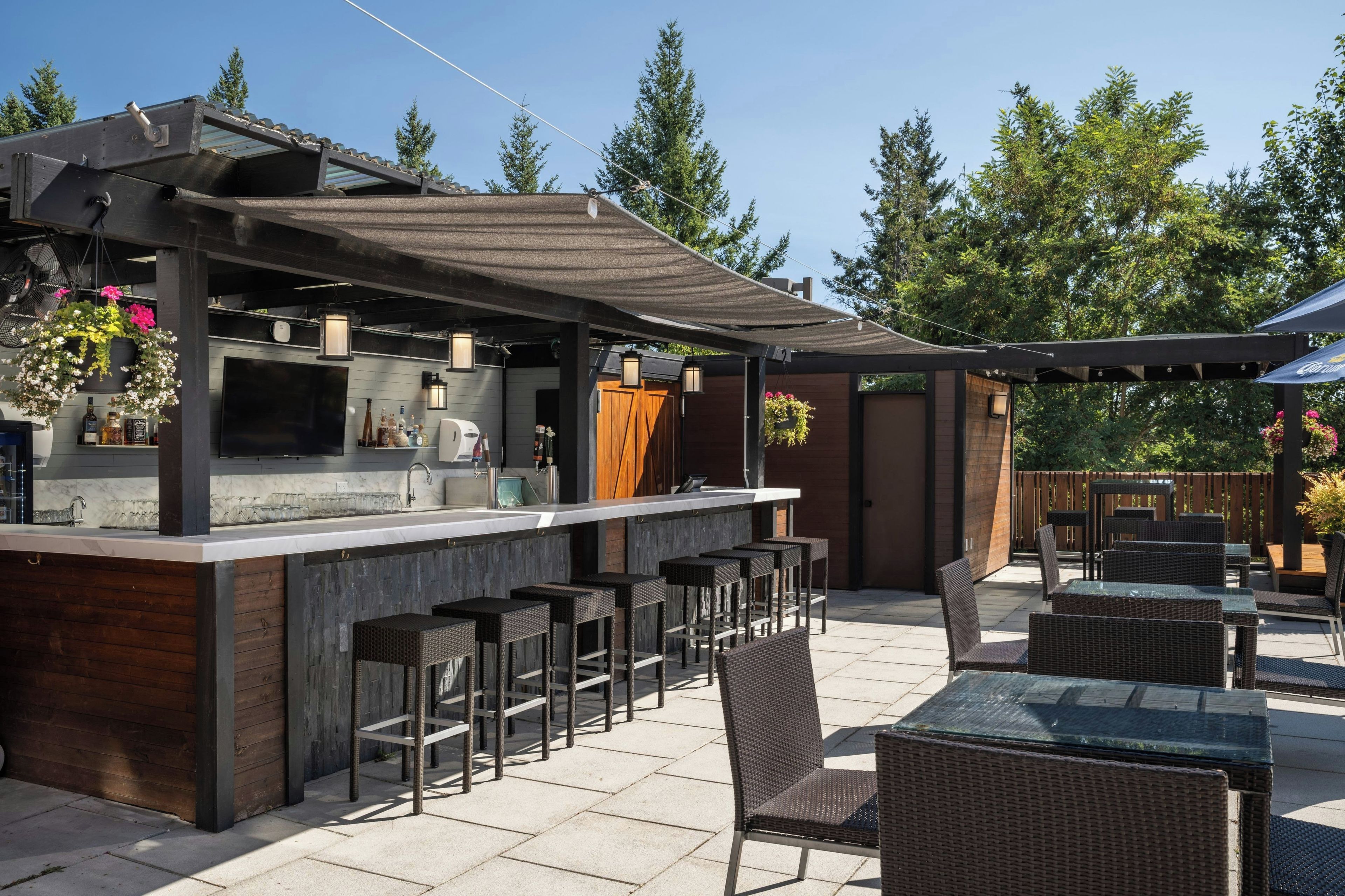 Un espace bar extérieur comprenant un comptoir, des tabourets et une pergola.