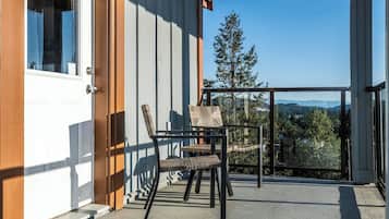 A covered balcony with a view of a mountain range, a wooden door, and two wicker chairs.
