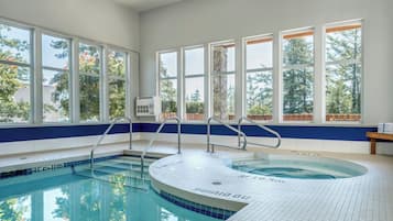 An indoor swimming pool with clear blue water, surrounded by large windows offering views of trees and a building.
