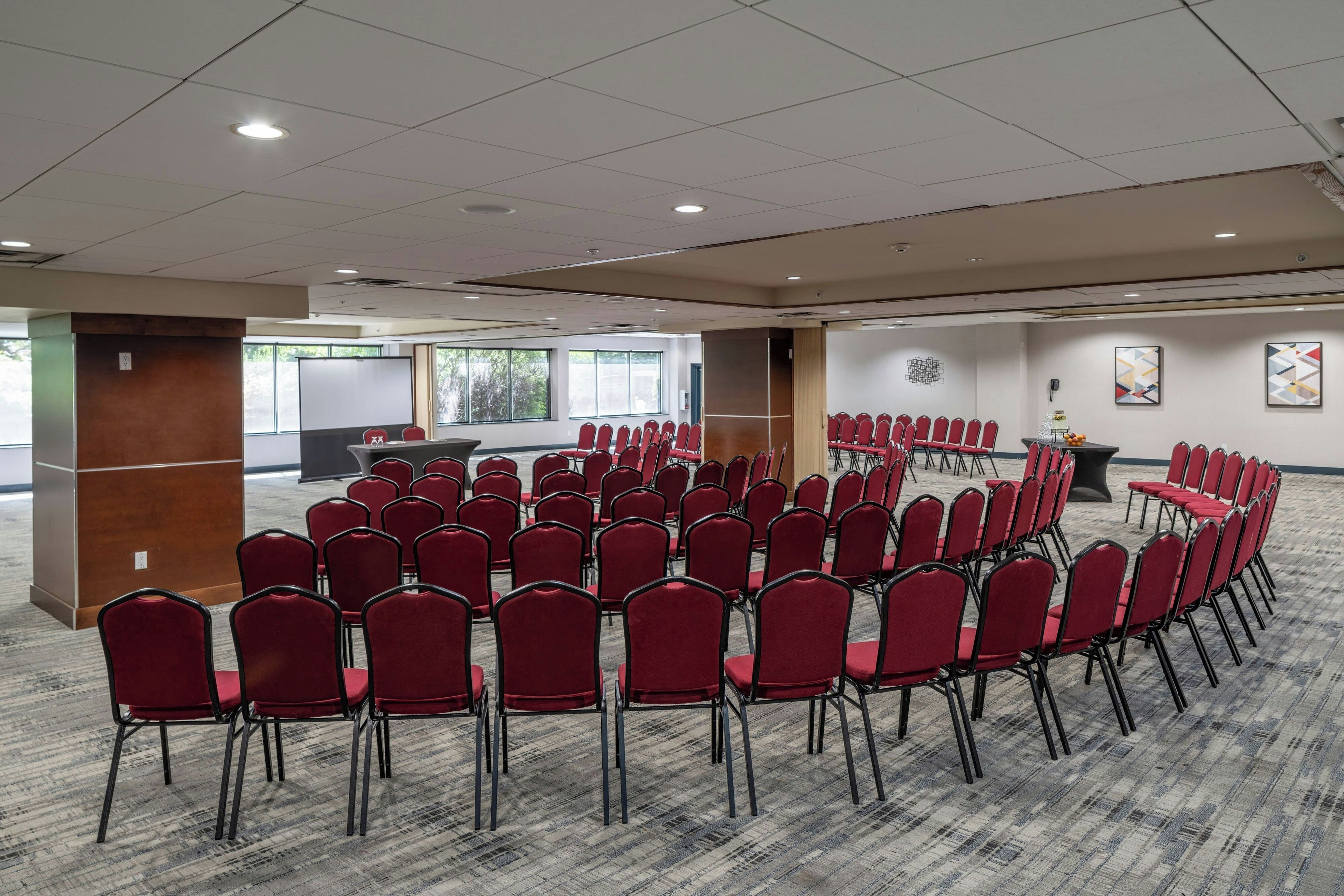Sala de conferência com cadeiras vermelhas dispostas em semicírculo, um quadro branco e uma tela de projeção.