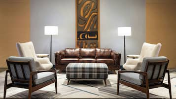Ein moderner Lounge-Bereich mit einer Ledersofa, zwei Sesseln, einem Vichy-Pouff und einem dekorativen Wandbild.