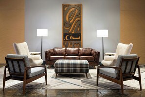 Un área de descanso moderna con un sofá de cuero, dos sillones, un reposapiés escocés y un adorno de pared.