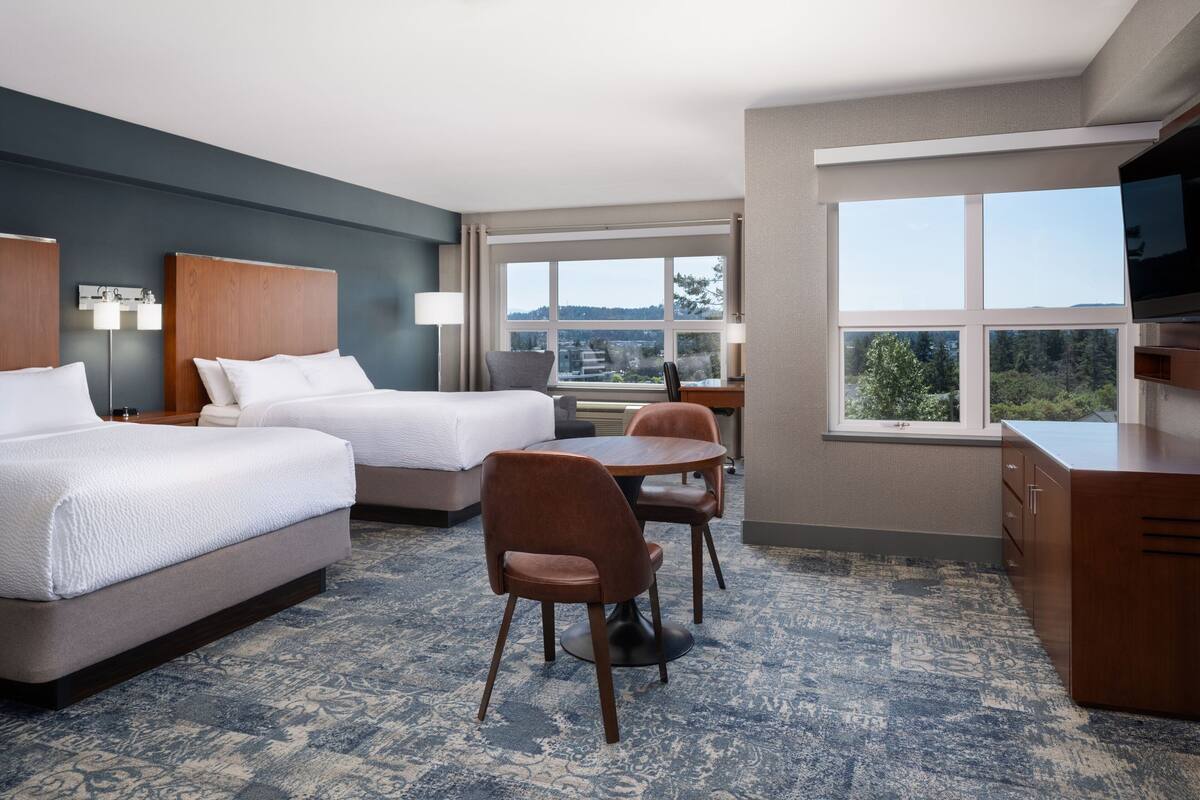 A hotel room with two beds, a dining table with chairs, a TV, and a view of the outdoors.