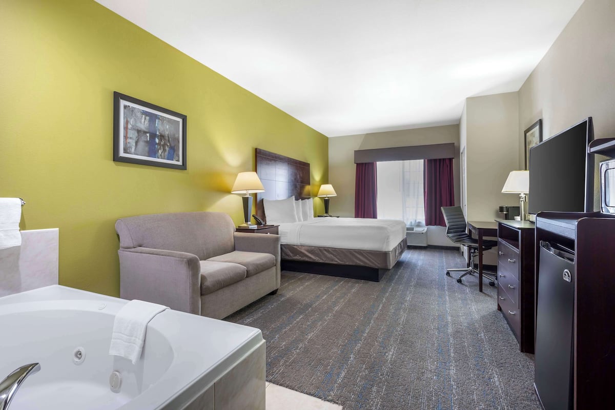A hotel room with a bed, a sofa, a desk, a TV, and a bathroom with a bathtub.
