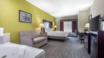 Quarto de hotel com cama, sofá, escrivaninha, televisão e banheiro com banheira.