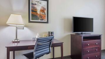 A hotel room with a desk, chair, television, and a cabinet.