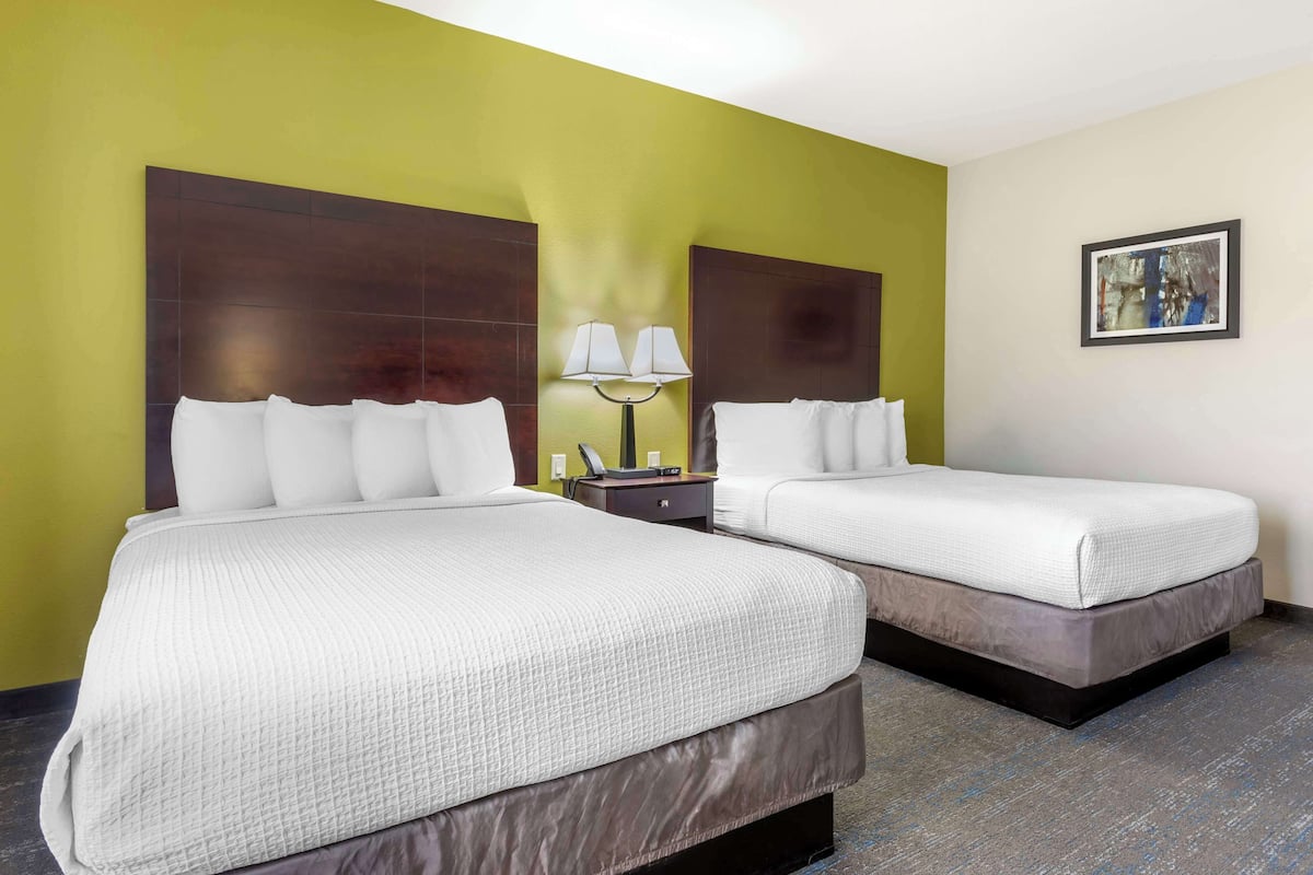 A hotel room with two beds, a nightstand with a lamp, and a painting on the wall.