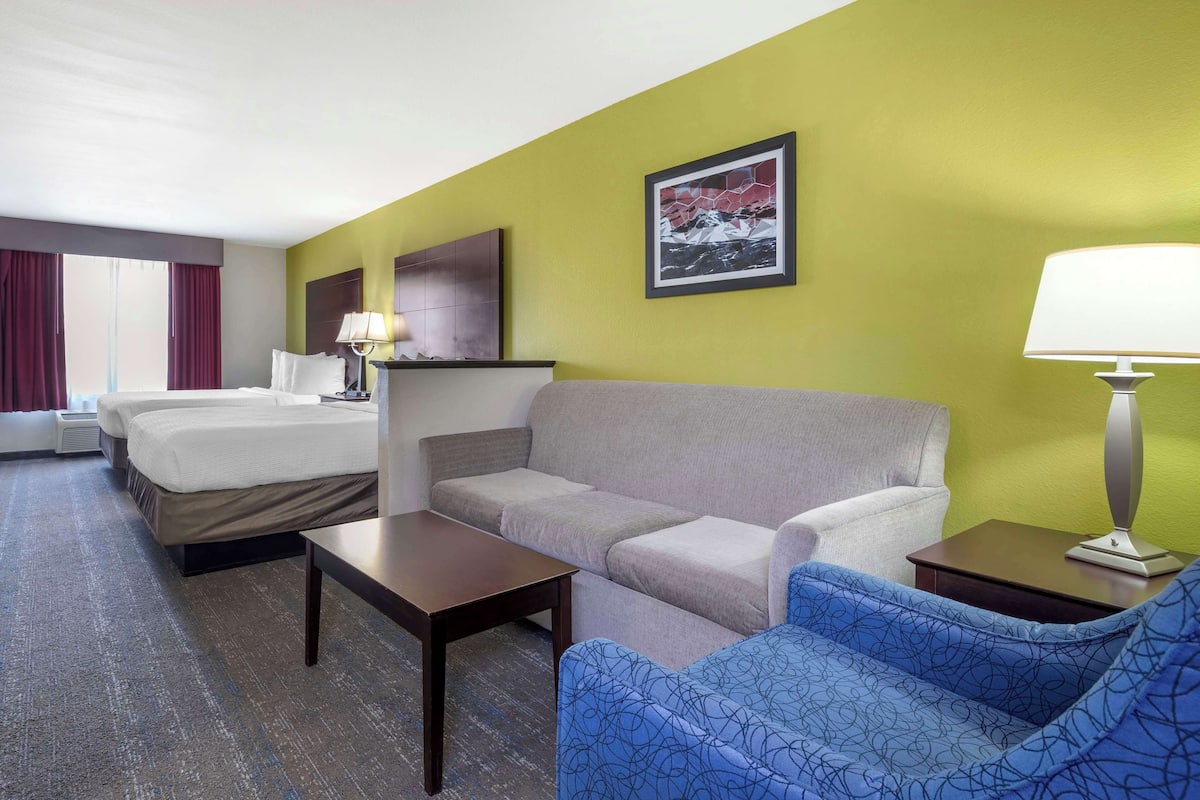 A hotel room with a bed, a sofa, a small table, a lamp, and a picture on the wall.