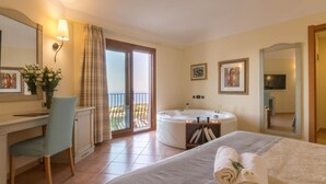 A hotel room with a bed, a desk, a chair, a bathtub, a balcony, and a TV. - Hotel Brancamaria (Dorgali)