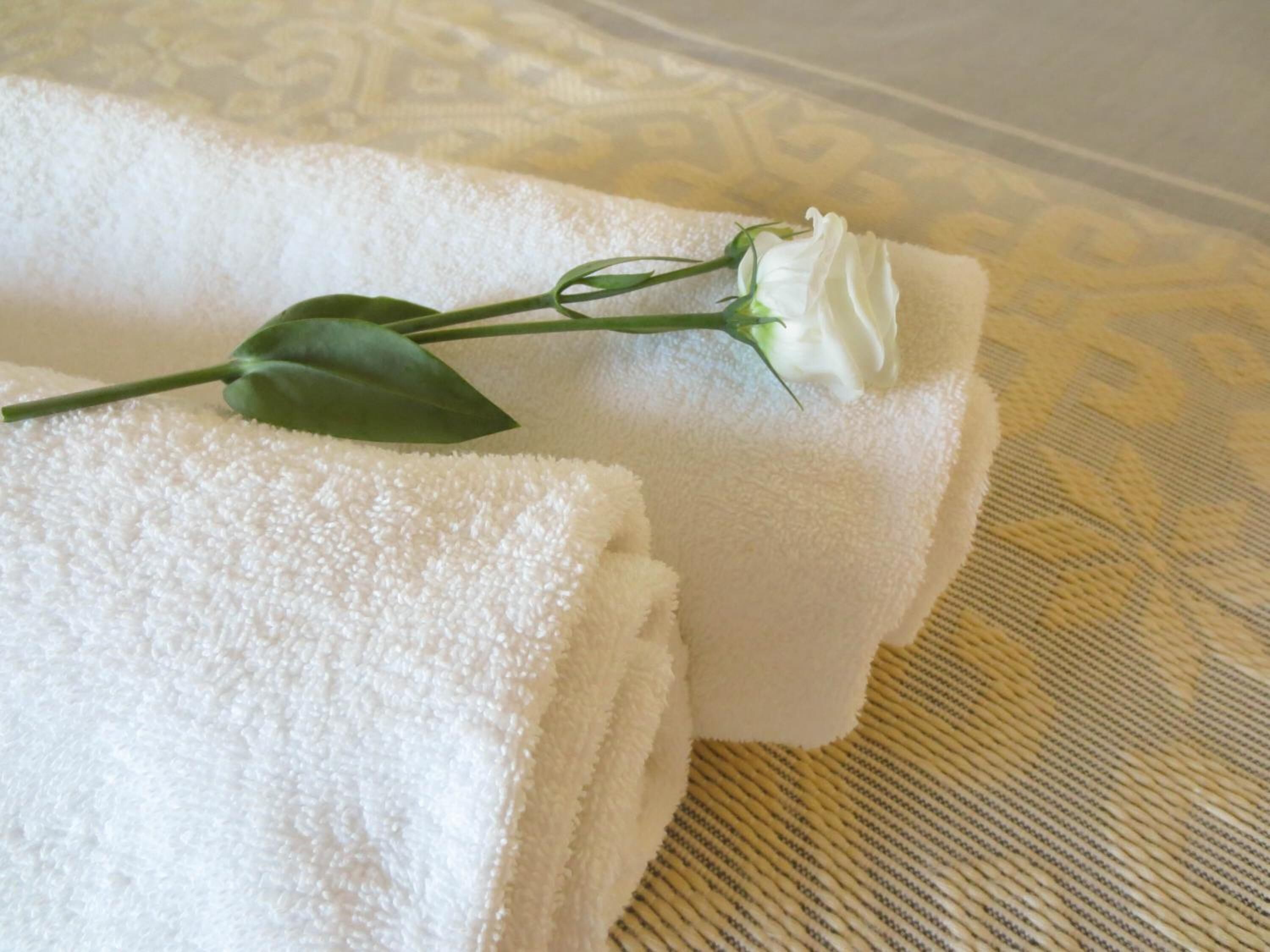 A stack of white towels and a white rose on a textured surface.