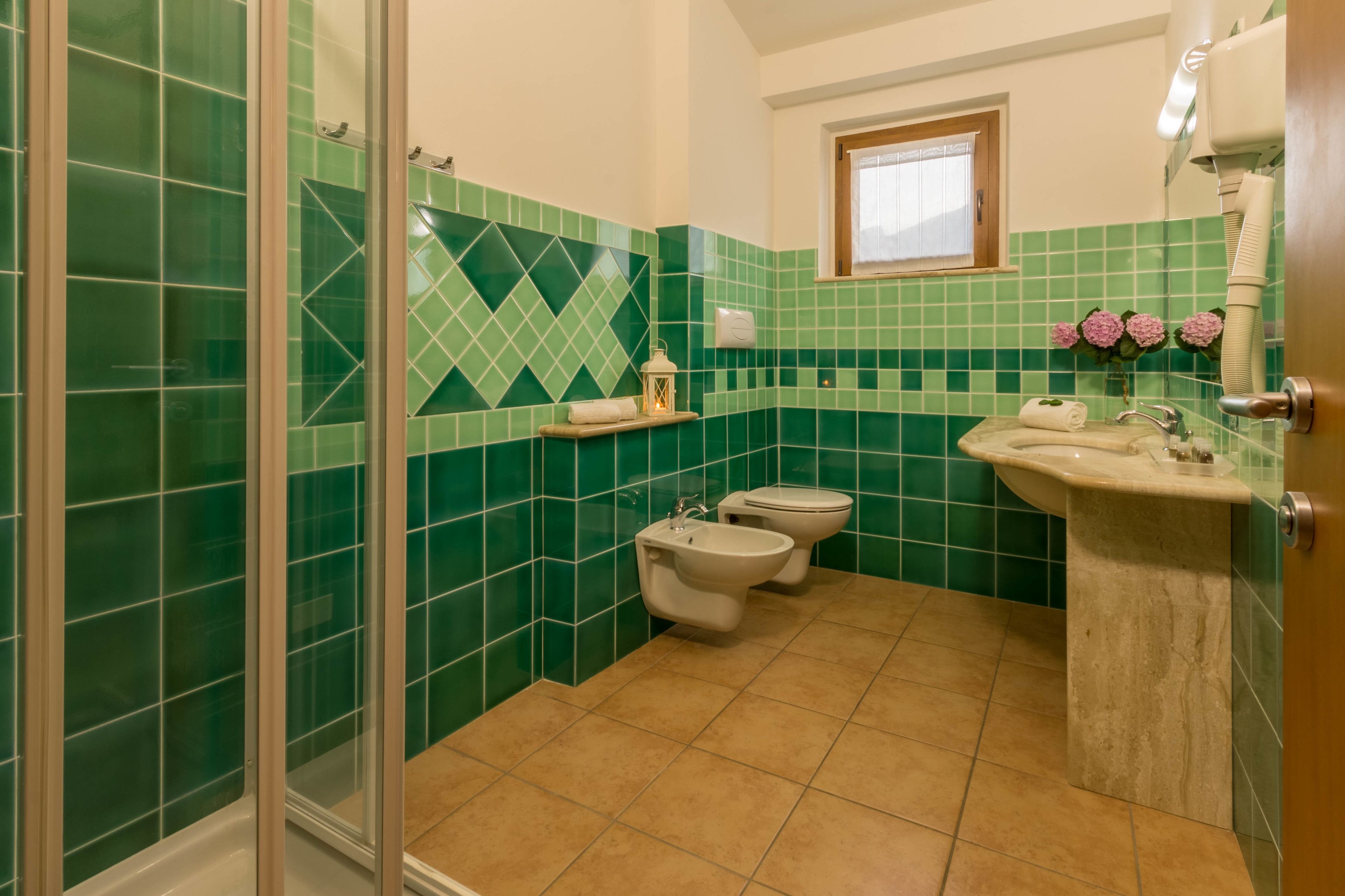 A bathroom with green tiles, a shower, a toilet, and a sink.
