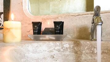 A bathroom vanity with a lit candle, two tubes of bath foam, and a faucet.