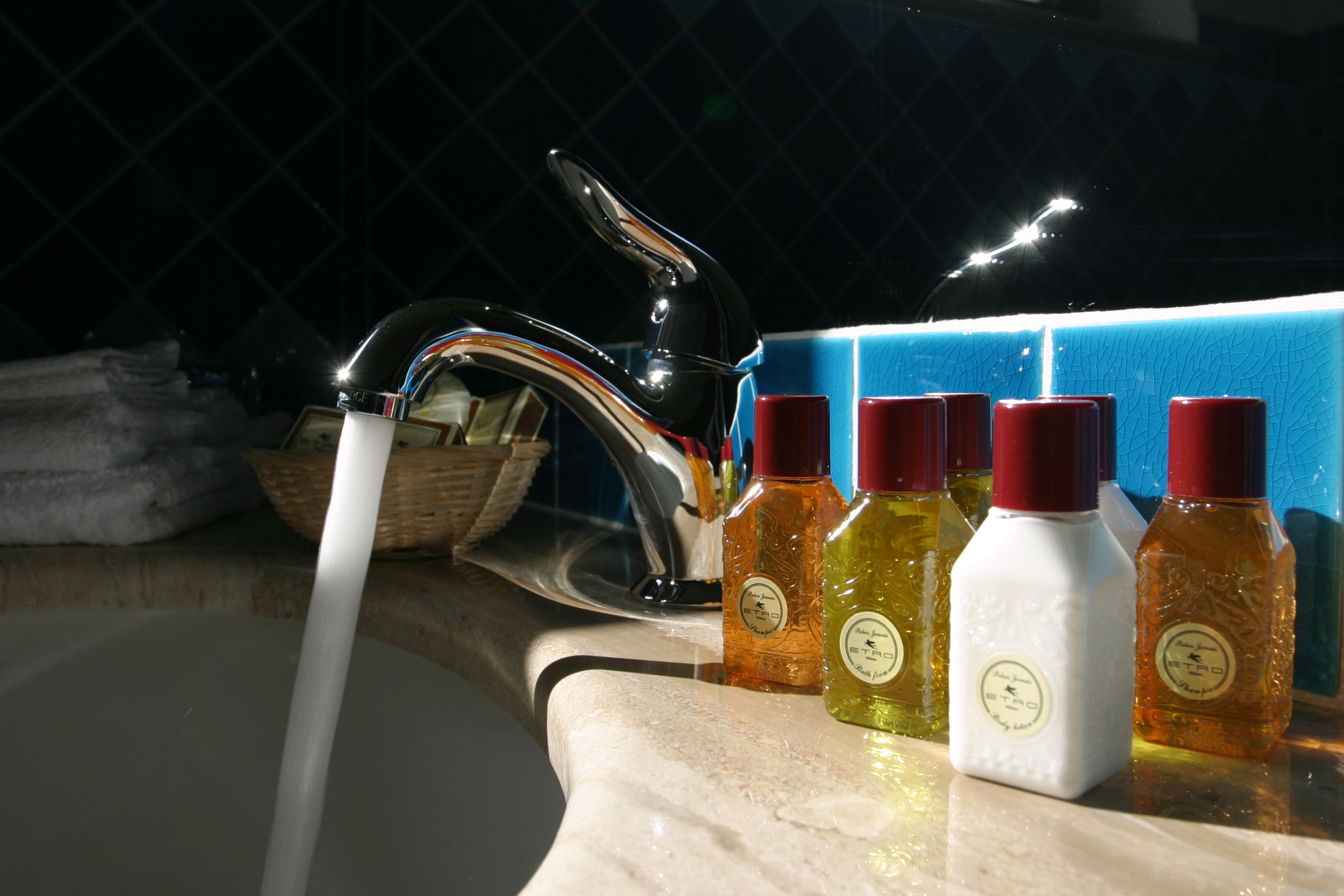 Un lavabo avec de l’eau courante, un miroir et quatre bouteilles de savon liquide.