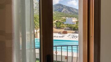 Vista de uma varanda com vista para uma piscina, com montanhas e edifícios ao fundo.
