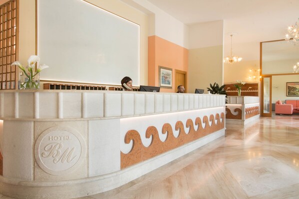 Un mostrador de recepción de hotel con diseño moderno, que incluye un piso de mármol y una zona de estar con un sofá rosa.