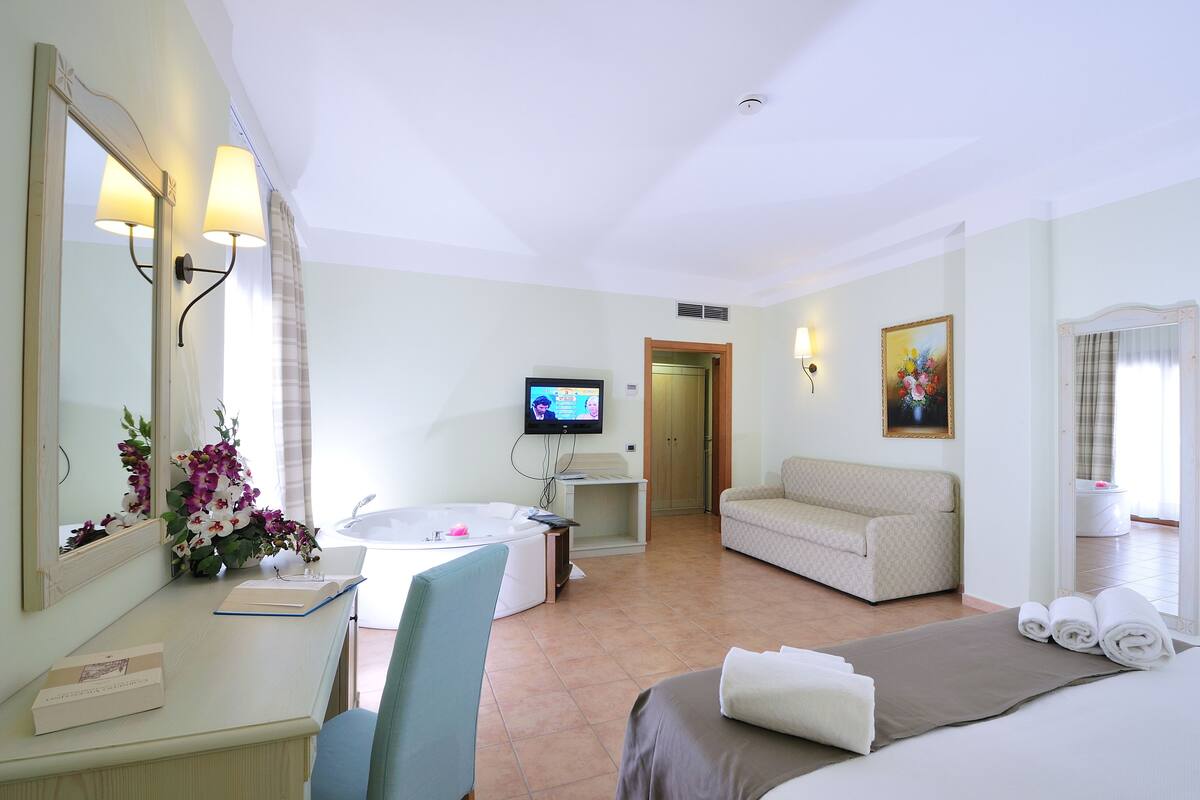 Habitación de hotel con cama, sofá, escritorio con computadora, televisión y baño con ducha.
