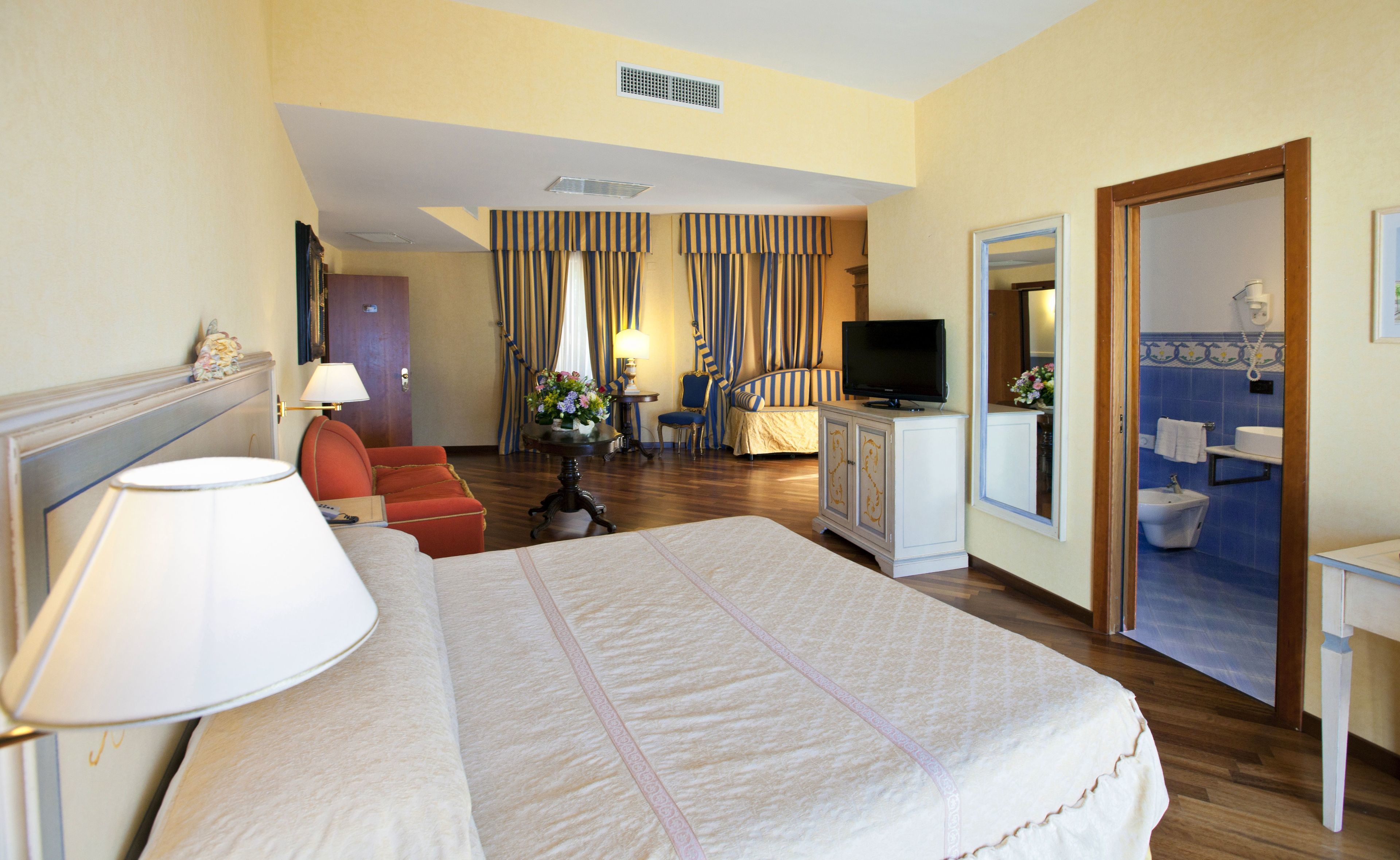 Camera d'albergo con un letto grande, una televisione, una scrivania e un bagno visibile attraverso una porta aperta.