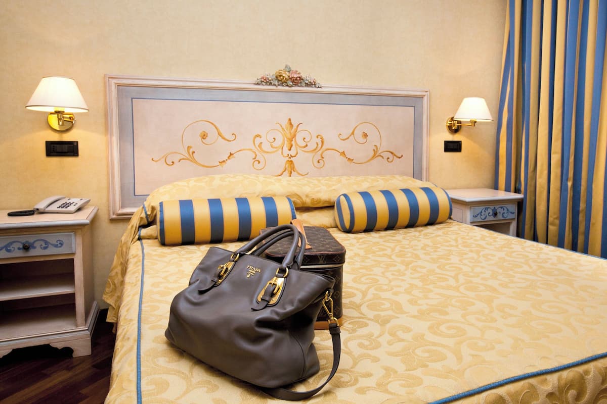 Una habitación de hotel con una cama grande, dos mesitas de noche, una lámpara, un teléfono y un bolso de mano.