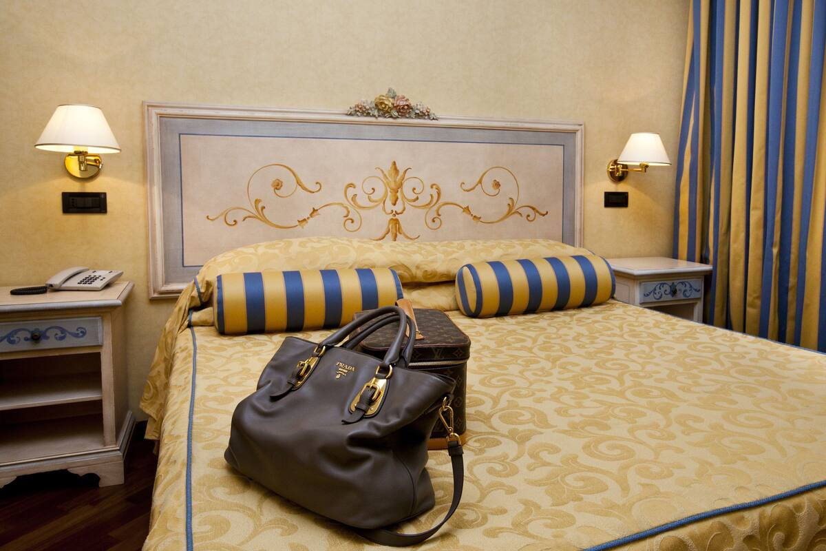 Camera d'albergo con un letto grande, due comodini, una lampada, un telefono e una borsa.