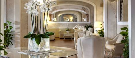 A glass-top table with a vase of white orchids, surrounded by white upholstered chairs in a well-lit, elegantly designed interior space.