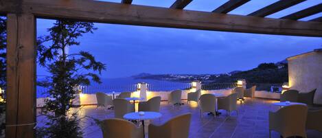 An outdoor patio with wicker furniture and a view of the sea at dusk.