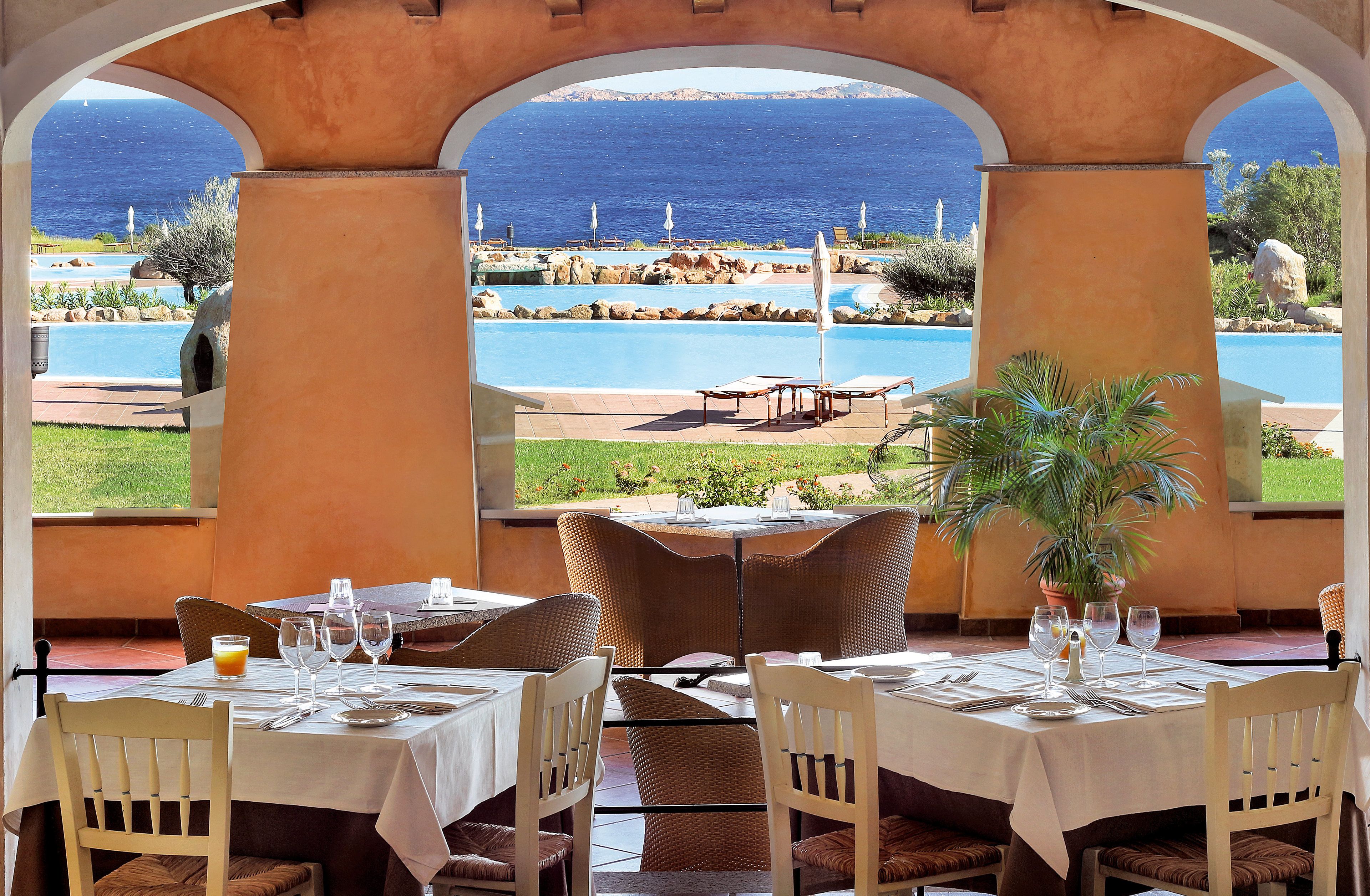 Un ristorante con tavoli all'aperto affacciato su una piscina e il mare.