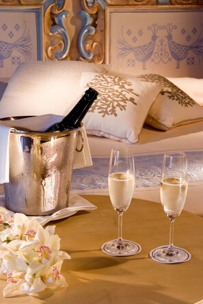 A champagne bucket with two glasses, a bouquet of flowers, and a bed with decorative pillows. - COLONNA RESORT, a Colonna Luxury Beach Hotel, Porto Cervo (Arzachena)